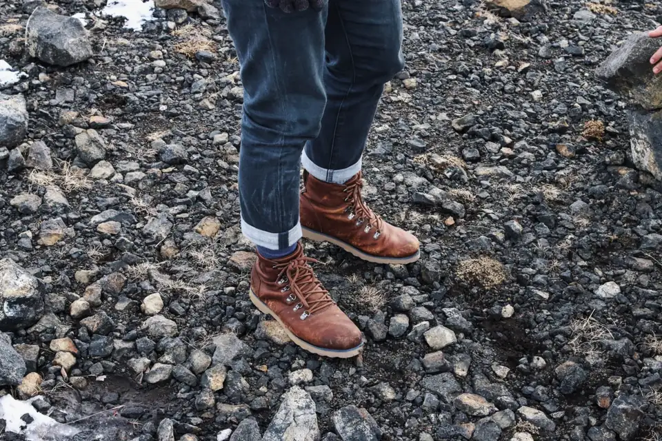 A walker in rolled jeans and brown leather lace-up hiking boots standing on rocky ground