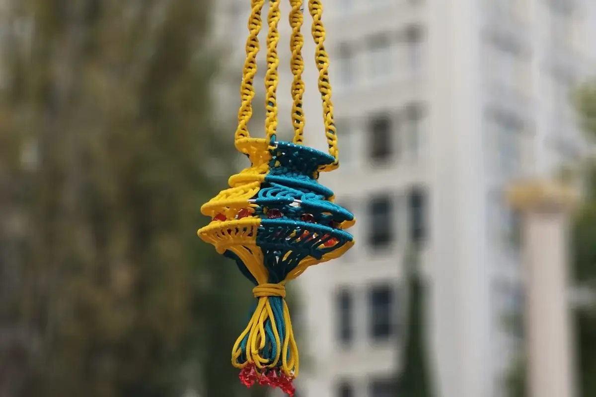 A macramé hanger in yellow and teal cord with spiral knot sections, hanging from a rope outdoors