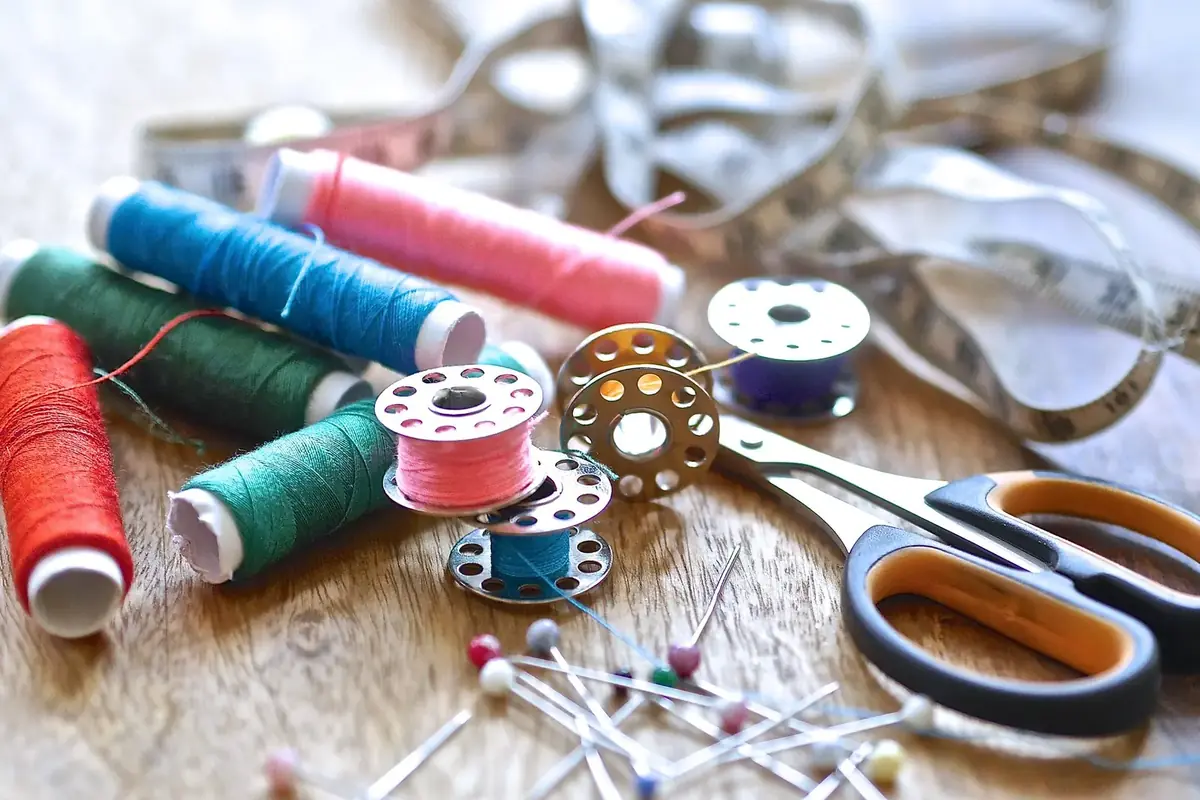 Spools of red, green, blue and pink thread with bobbins, pins, scissors and a tape measure on a wooden table