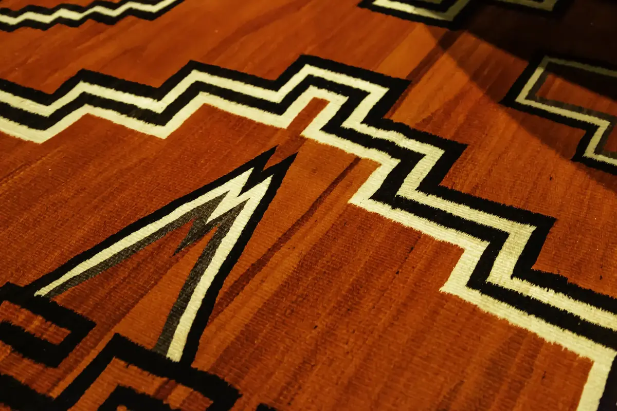 Close-up of a hand-woven rug with a deep red ground and stepped black, white and grey zigzag bands