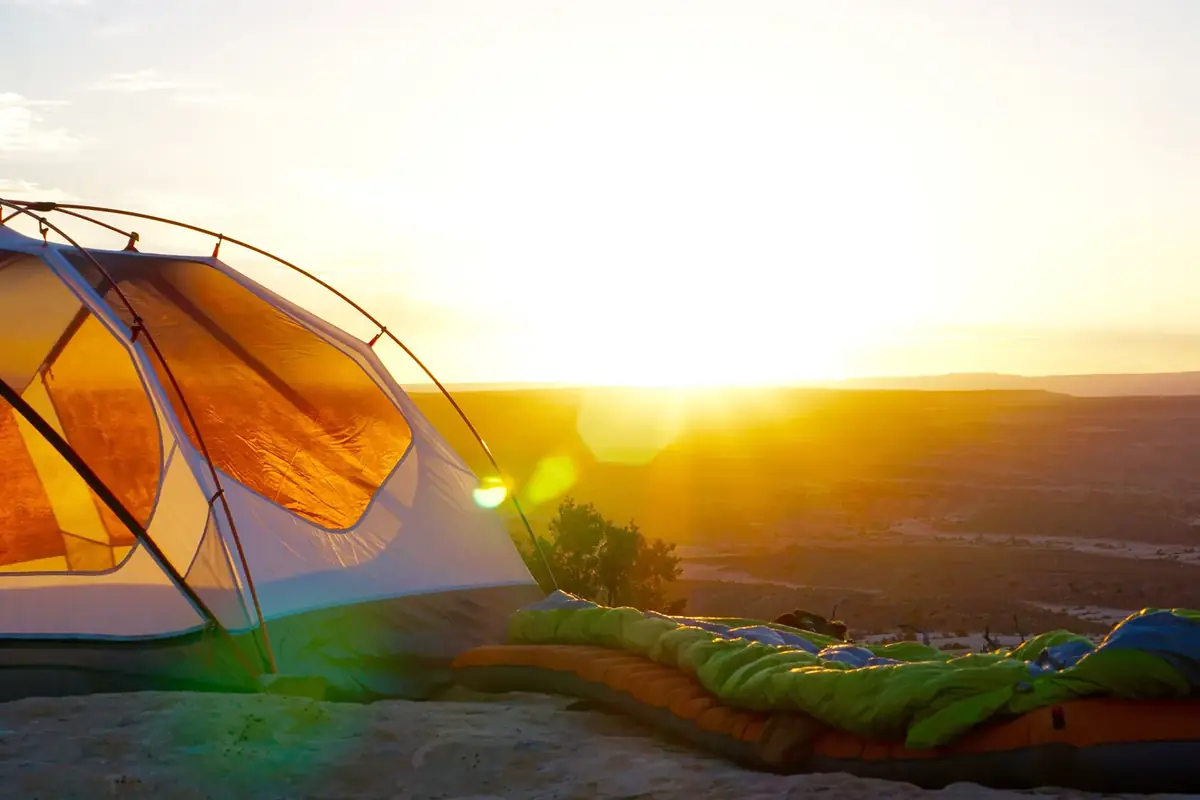 A small tent lit by the low sun on a rocky rim, with a sleeping bag laid out on a pad beside it