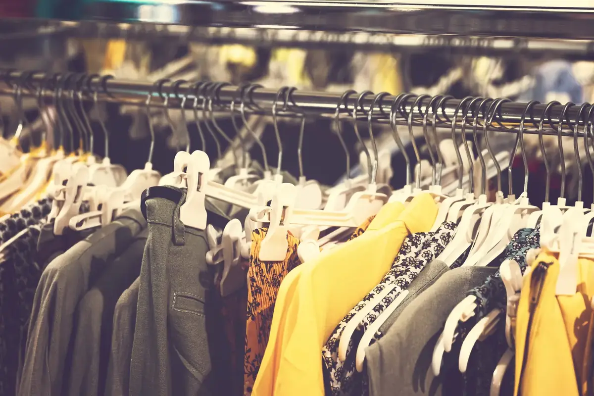 Shirts, jackets and dresses in grey, mustard and floral prints on white hangers along a shop rail