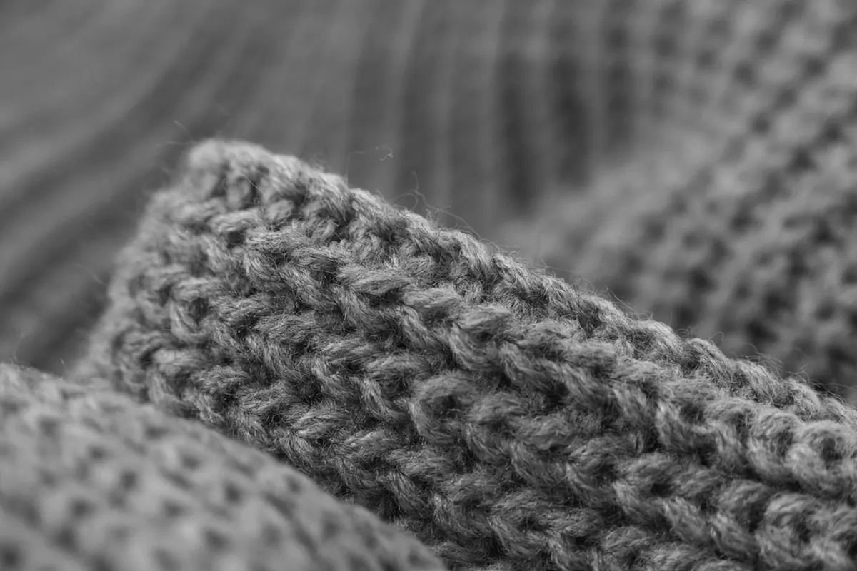 Close-up of a chunky grey knitted sweater folded over on itself, with soft out-of-focus knit behind